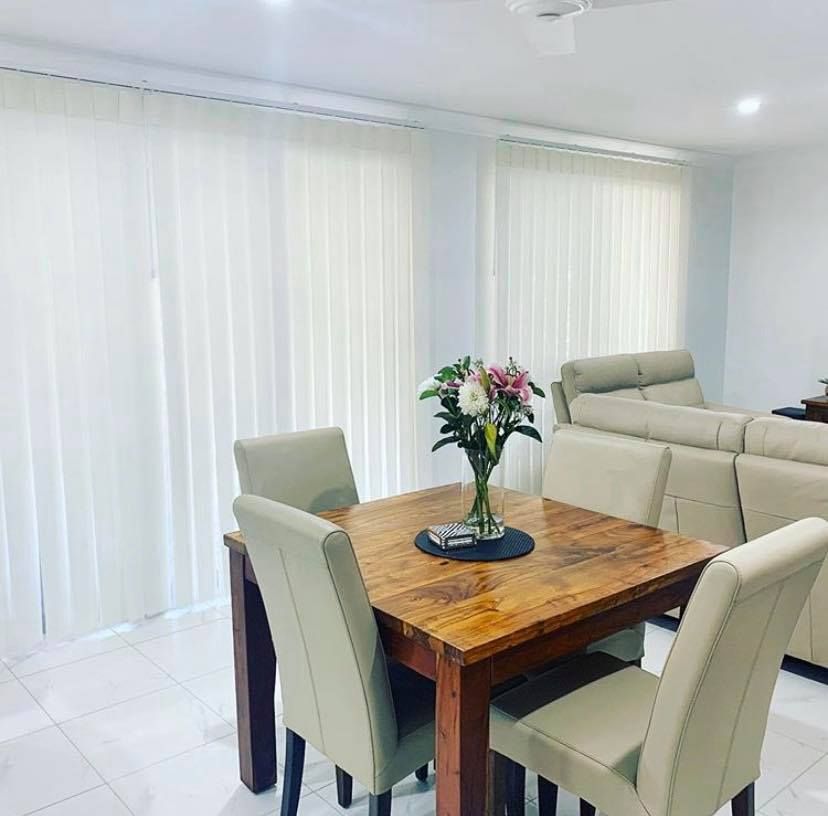 Office room with two windows. Beige roller shades, patterned dark screens, green trees, city view.