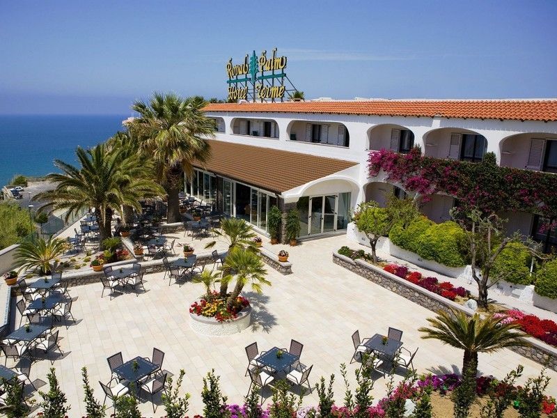 Hotel con patio esterno con vista sul mare, palme e fiori.