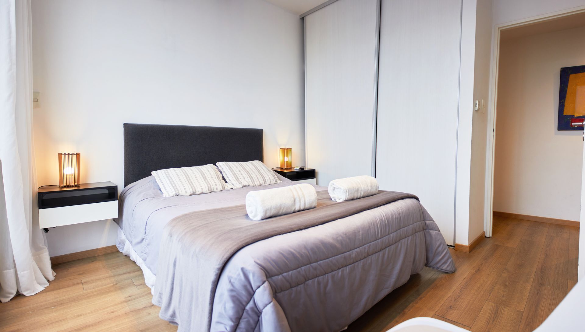 Dormitorio moderno con colcha gris, lámparas de noche y puertas correderas blancas en el armario.