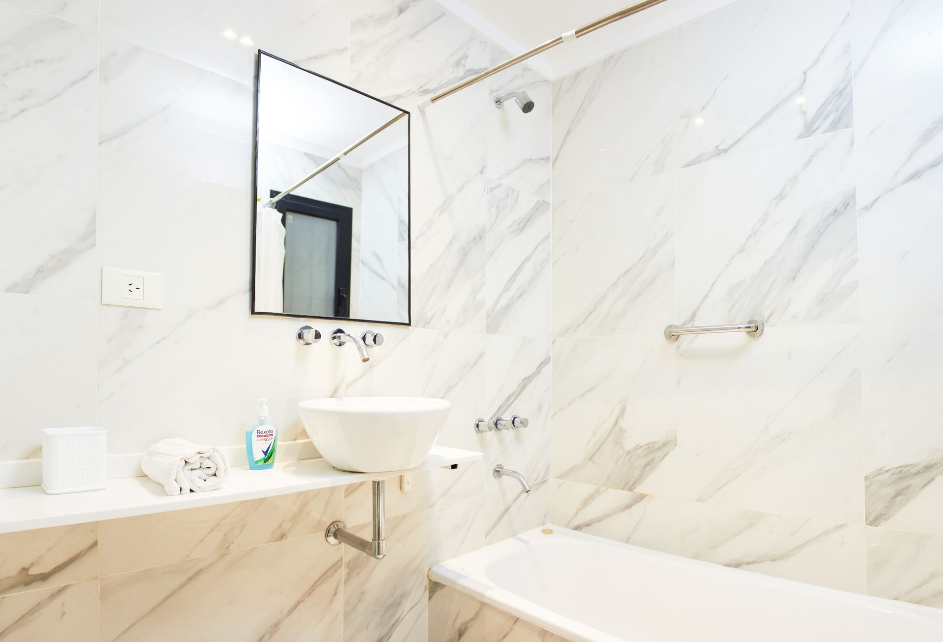 Baño moderno y luminoso de color blanco con paredes, lavabo, espejo y bañera de mármol.