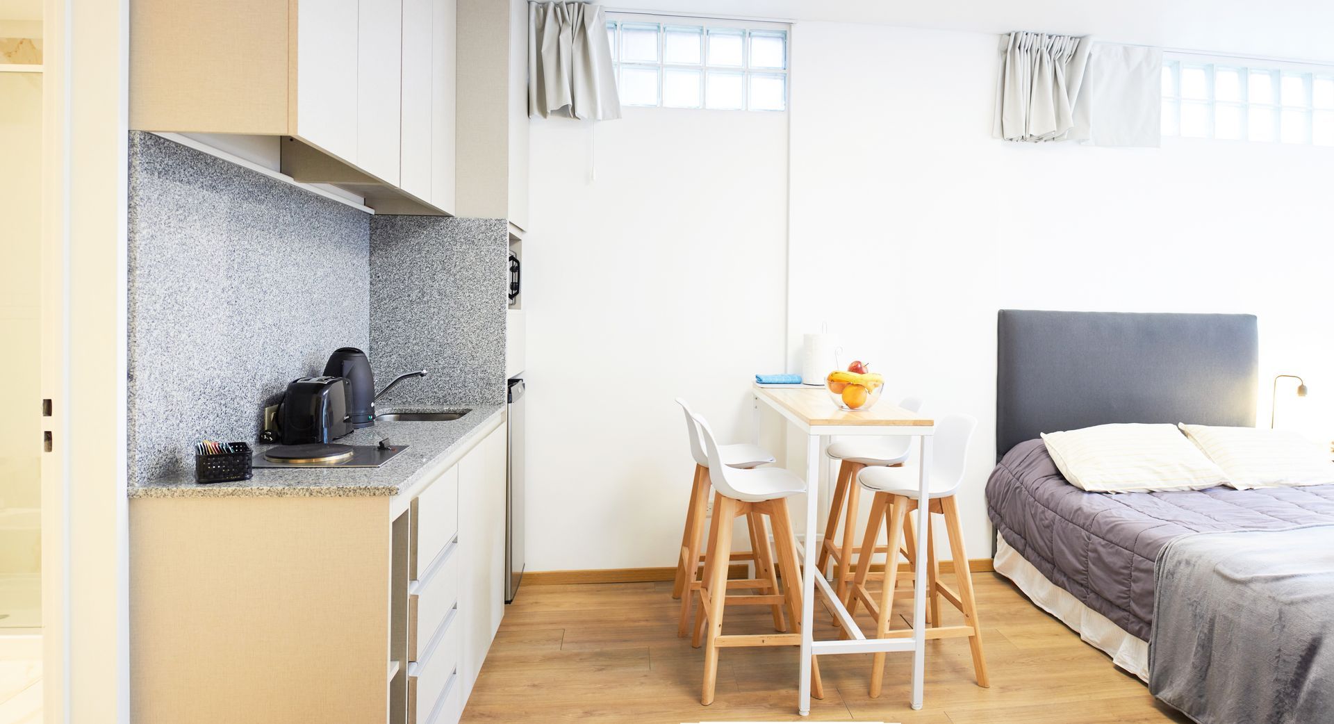 Estudio luminoso con cocina americana, mesa de comedor pequeña y cama junto a la ventana.