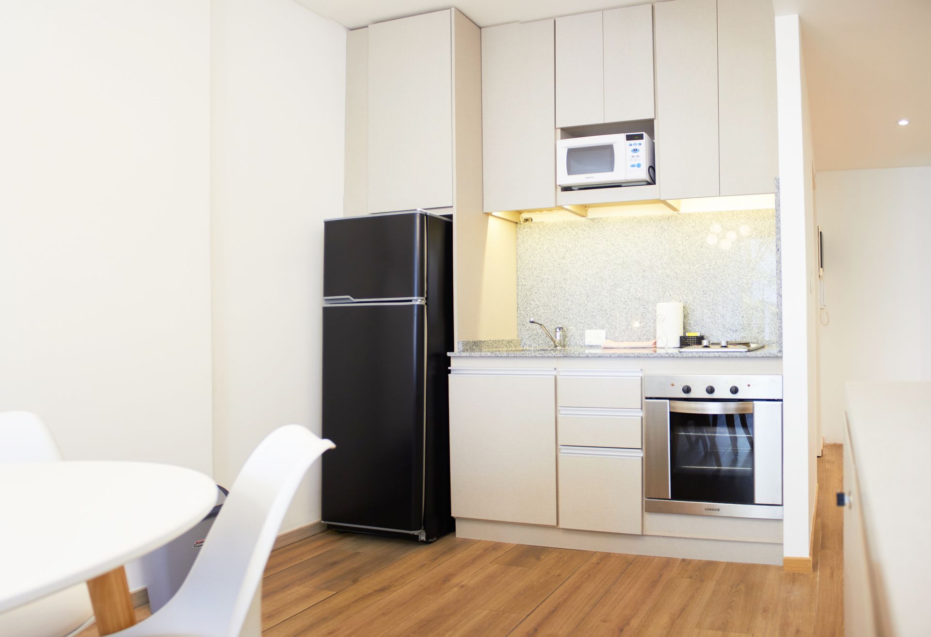 Cocina moderna blanca con nevera negra, horno de acero inoxidable y suelo de madera.