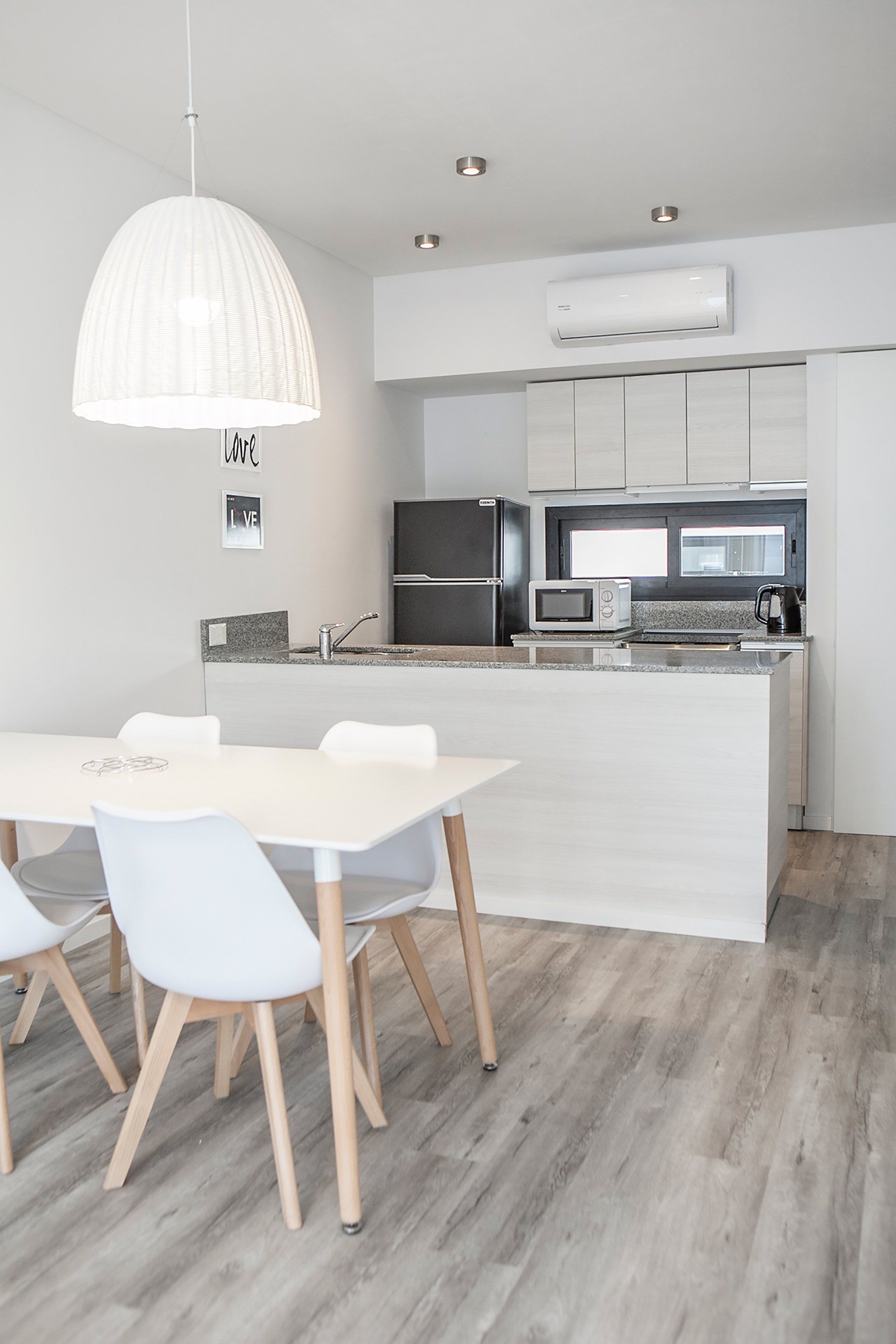 Cocina y comedor modernos y luminosos con muebles blancos, lámpara colgante y suelo de madera.