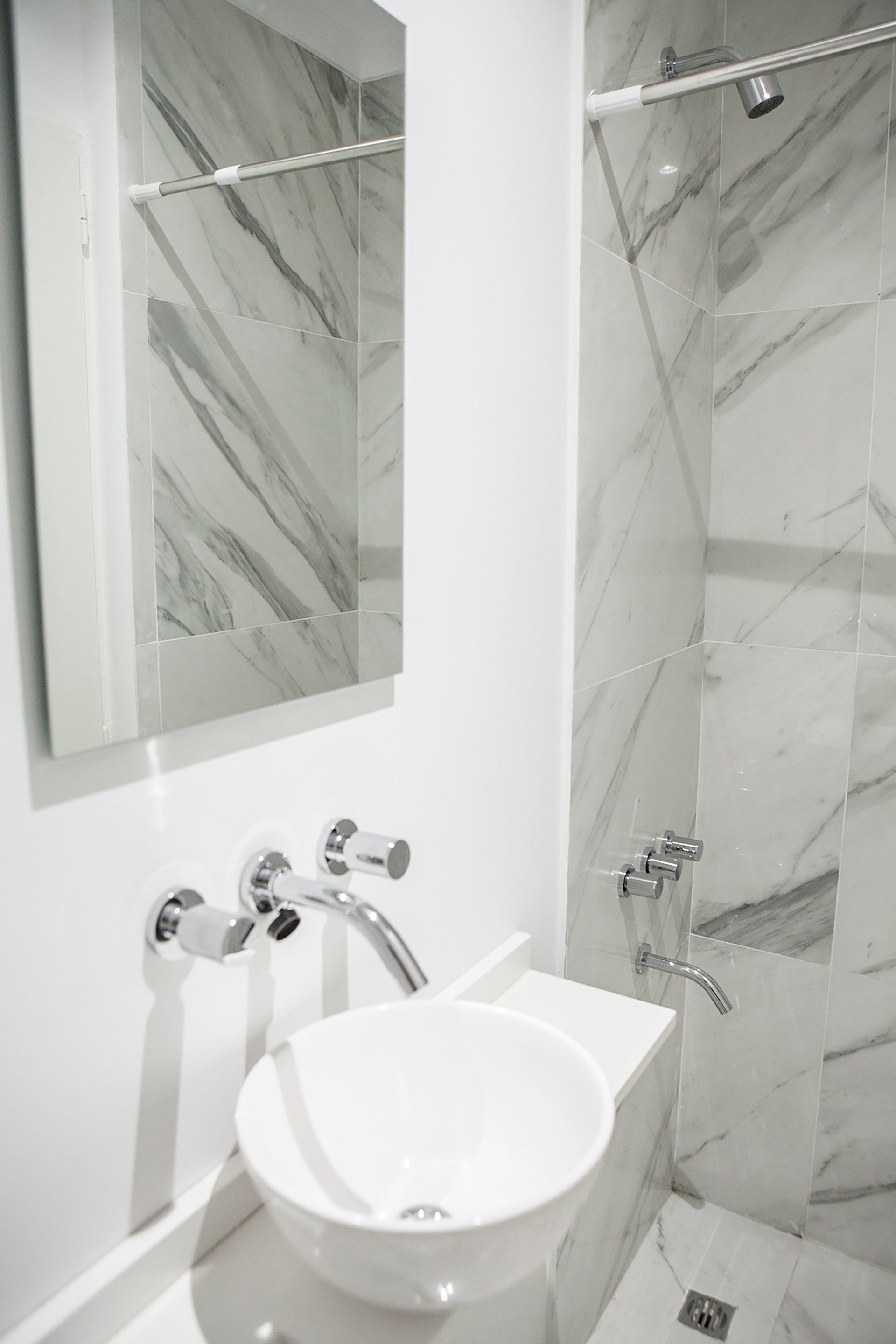 Lavabo moderno con grifería cromada, lavabo redondo blanco, espejo y paredes revestidas de mármol.