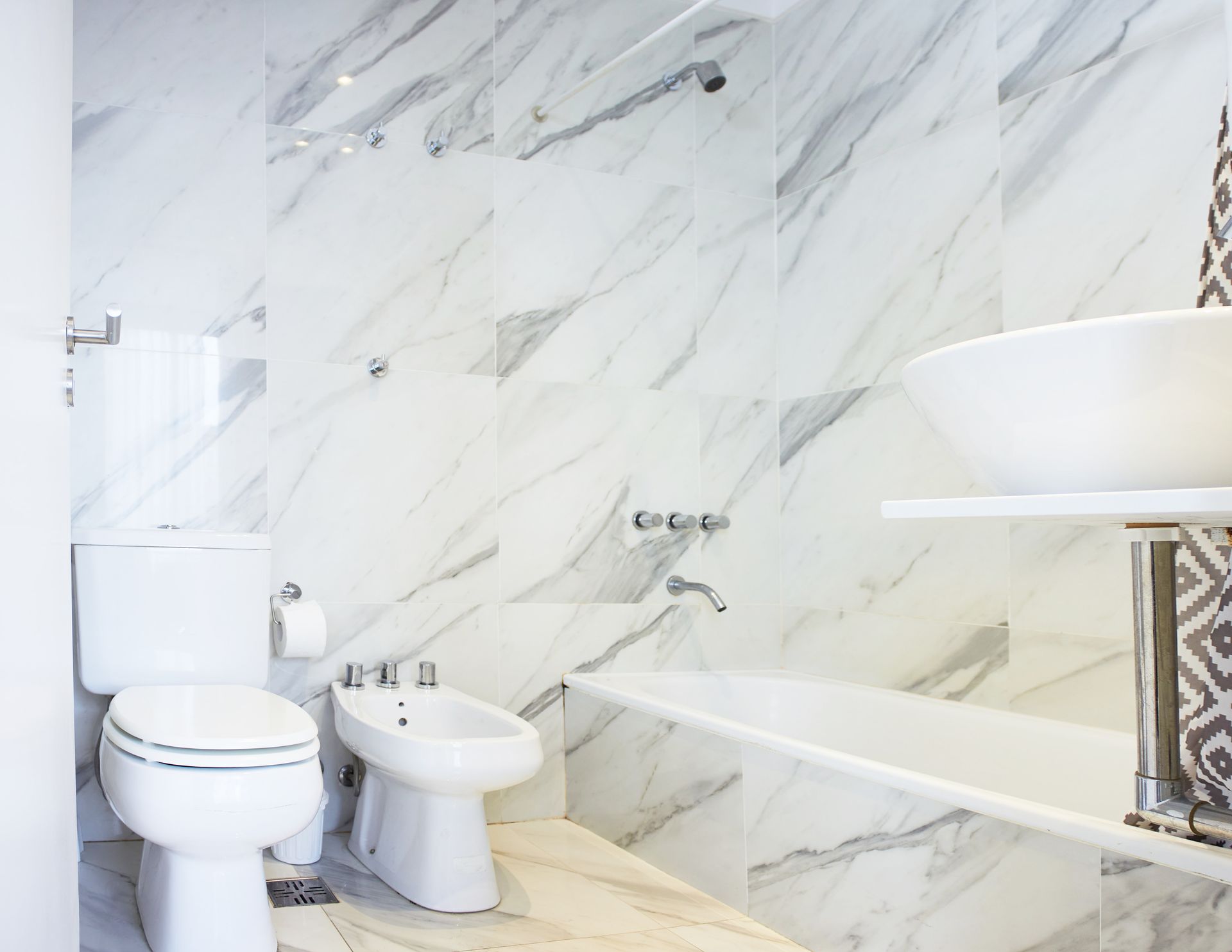 Baño moderno con paredes de mármol blanco, inodoro, bidé, bañera y lavabo.