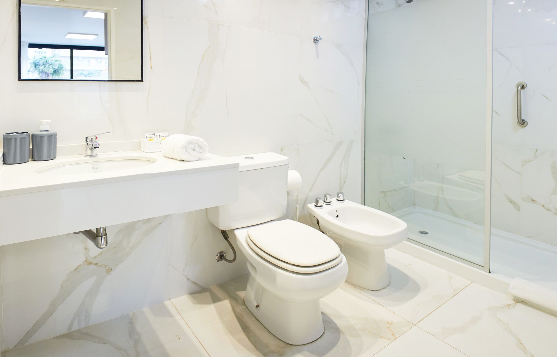 Baño moderno blanco con inodoro, bidé, lavabo, espejo y cabina de ducha de cristal.