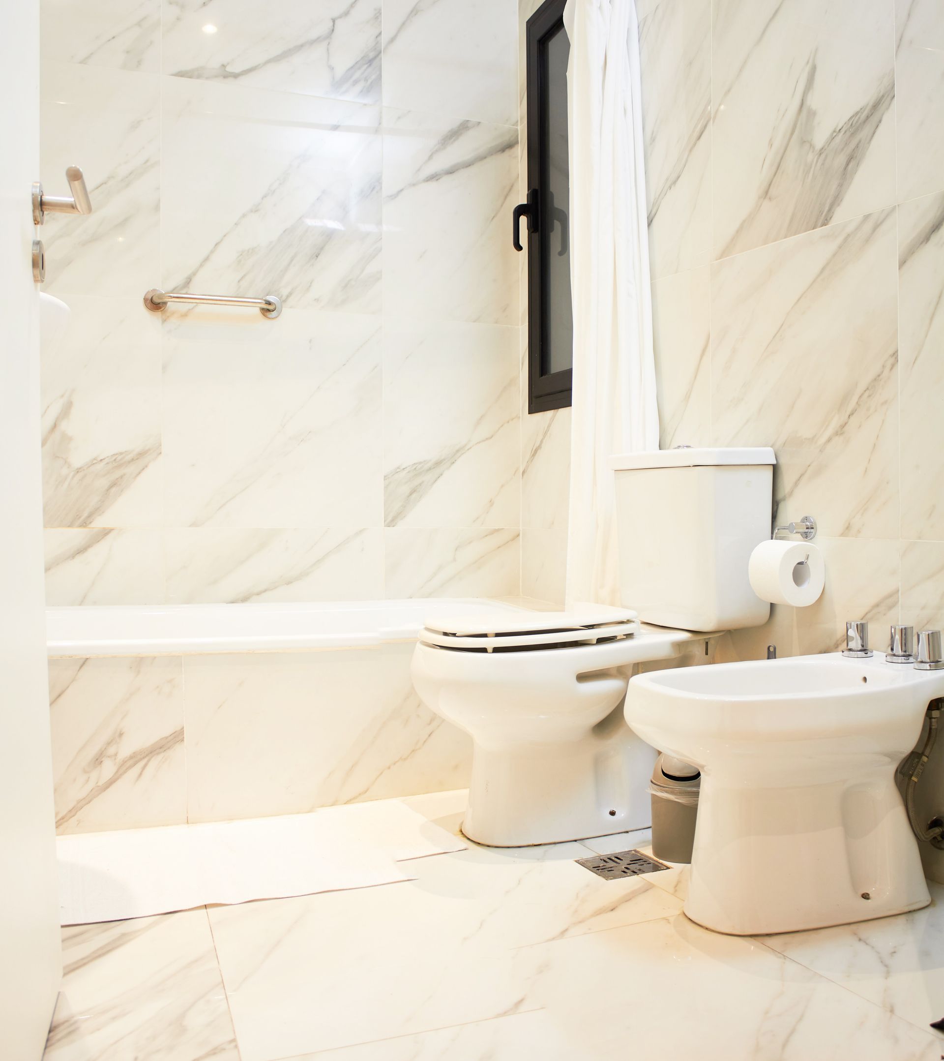 Baño moderno con azulejos de mármol, inodoro, bidé y controles de ducha montados en la pared.
