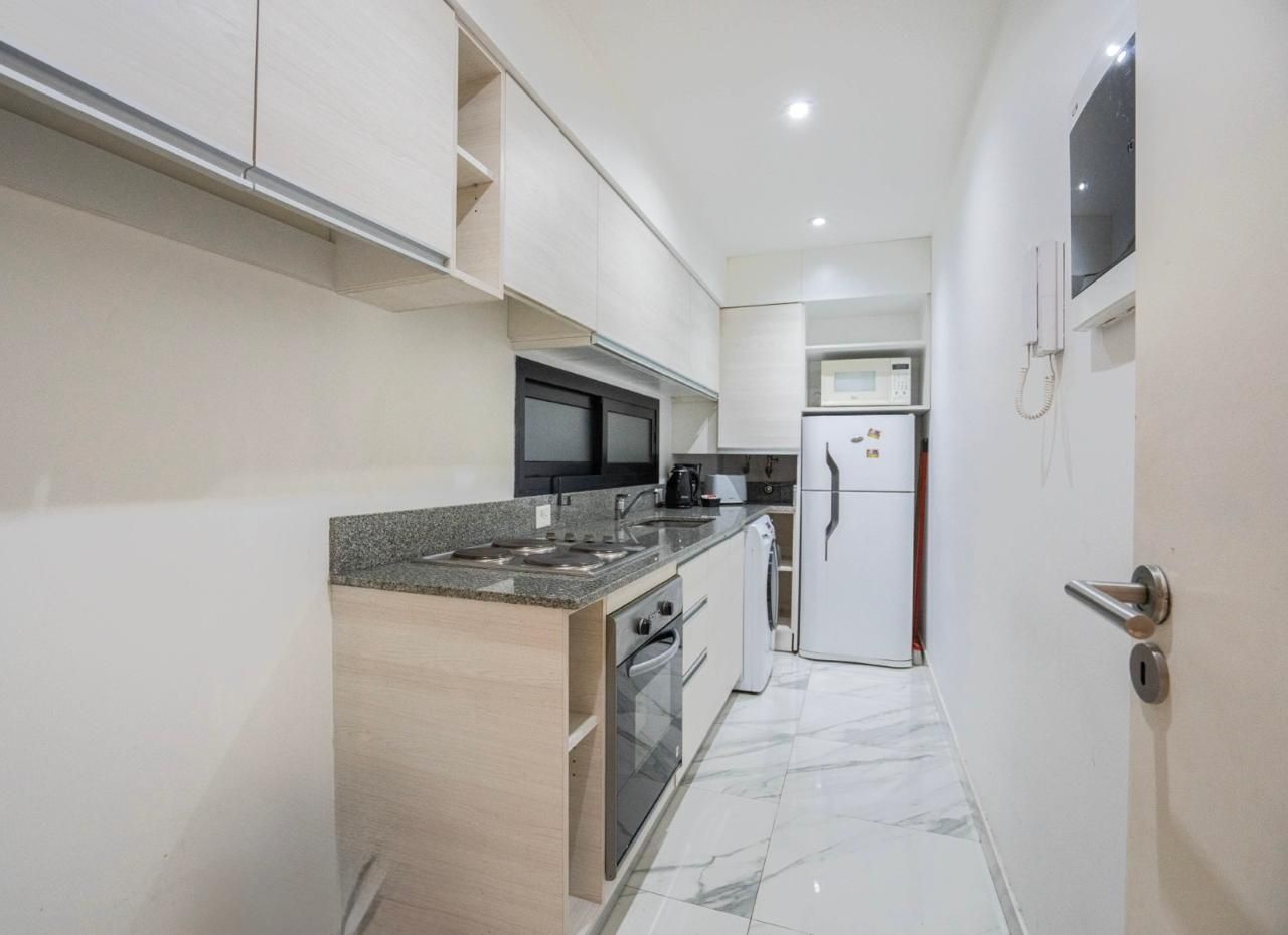 Cocina estrecha tipo galera blanca con encimeras de granito, microondas, estufa y refrigerador bajo luces empotradas.
