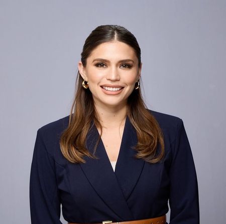 A woman wearing a green jacket and a pearl necklace is smiling for the camera.