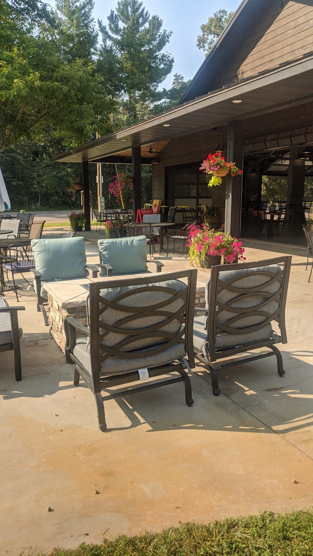 Outdoor patio with tables, chairs, and pink flower pots beside a building and trees.