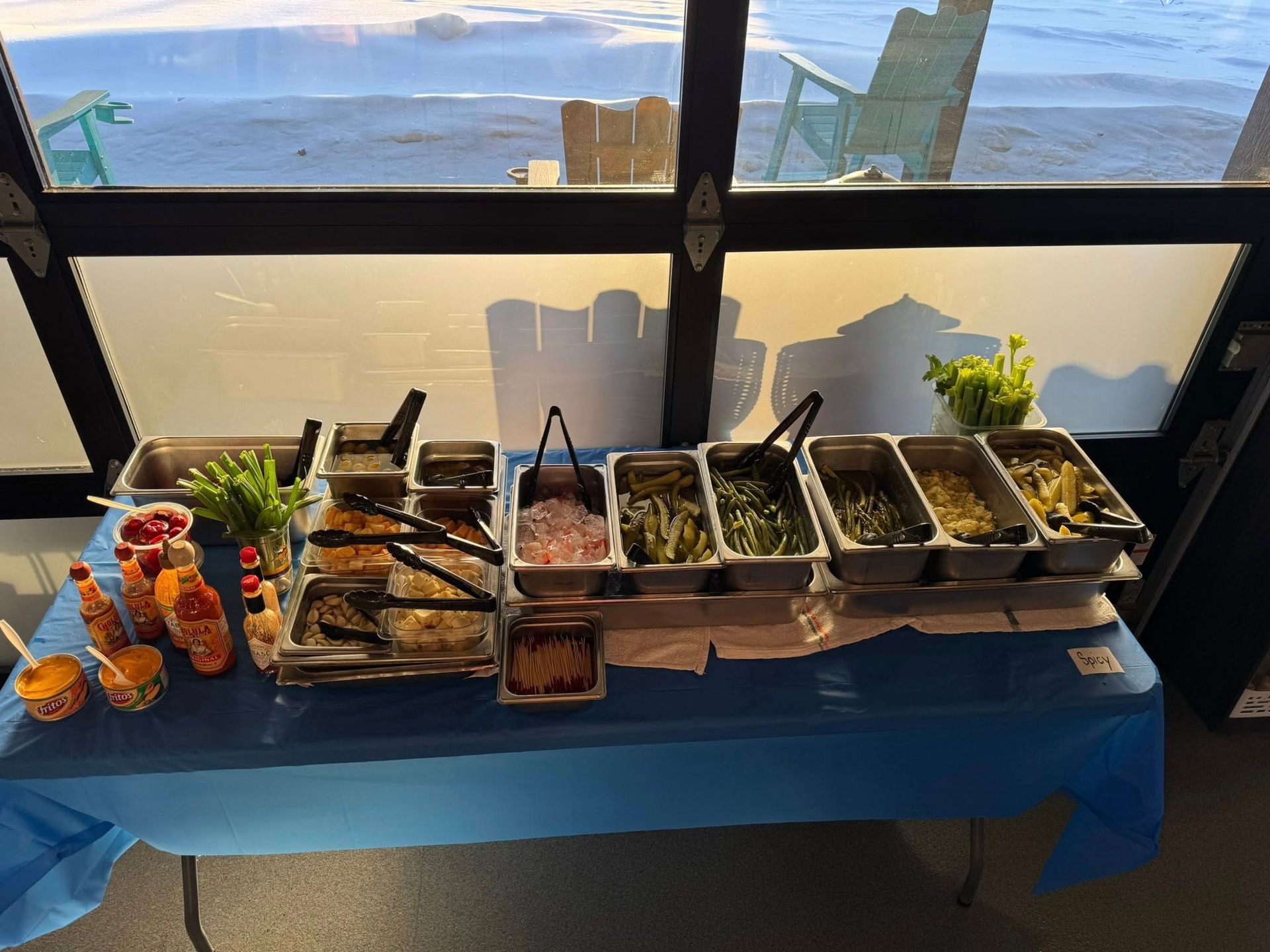 Buffet table with assorted food trays and plants beside a large window overlooking the water