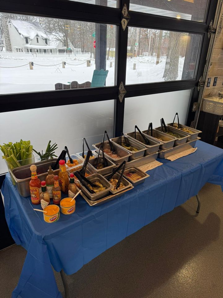 Snack table with trays of toppings and drinks on a blue tablecloth by snowy windows