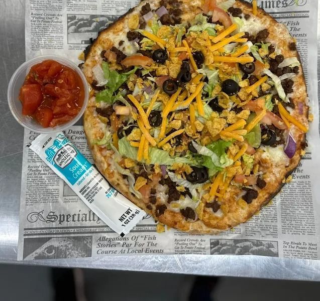 Vegetable pizza on newspaper with a small cup of salsa and a condiment packet beside it