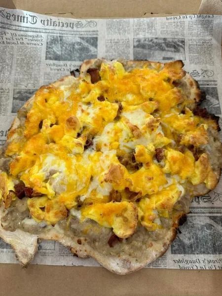 Cheesy pizza on newspaper, with a browned, irregular crust and melted yellow-orange topping