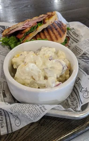 Sandwich and creamy potato salad in a white bowl on newspaper-lined tray