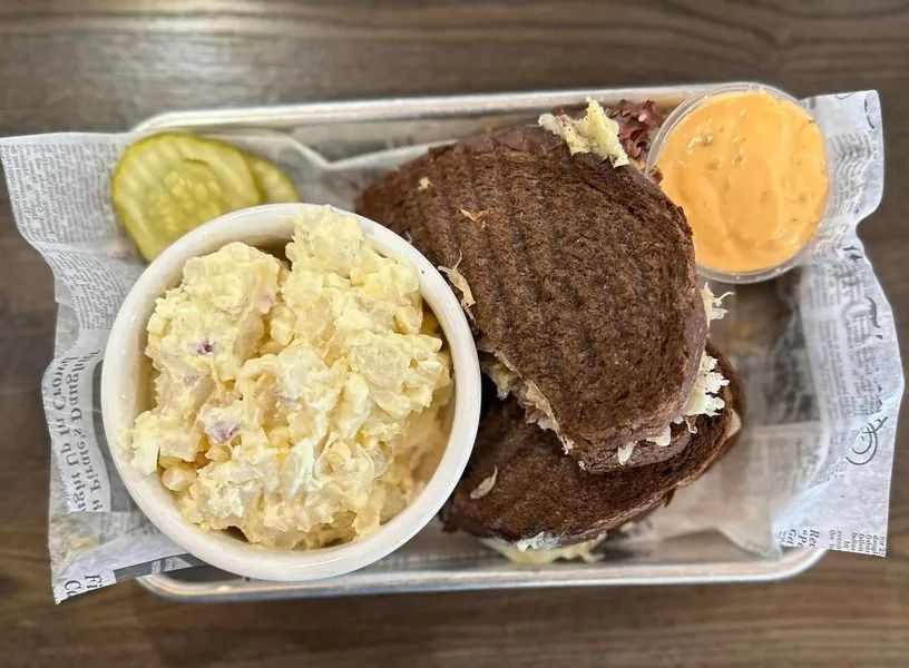Burger meal in a foil tray with potato salad, pickles, and orange dipping sauce