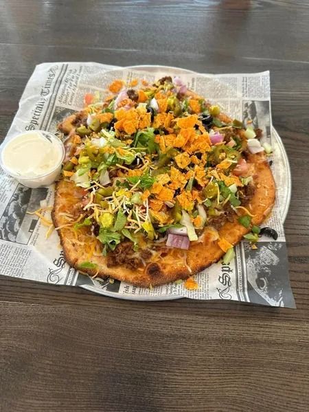 Loaded vegetable pizza on newspaper-lined tray with a small cup of white dipping sauce