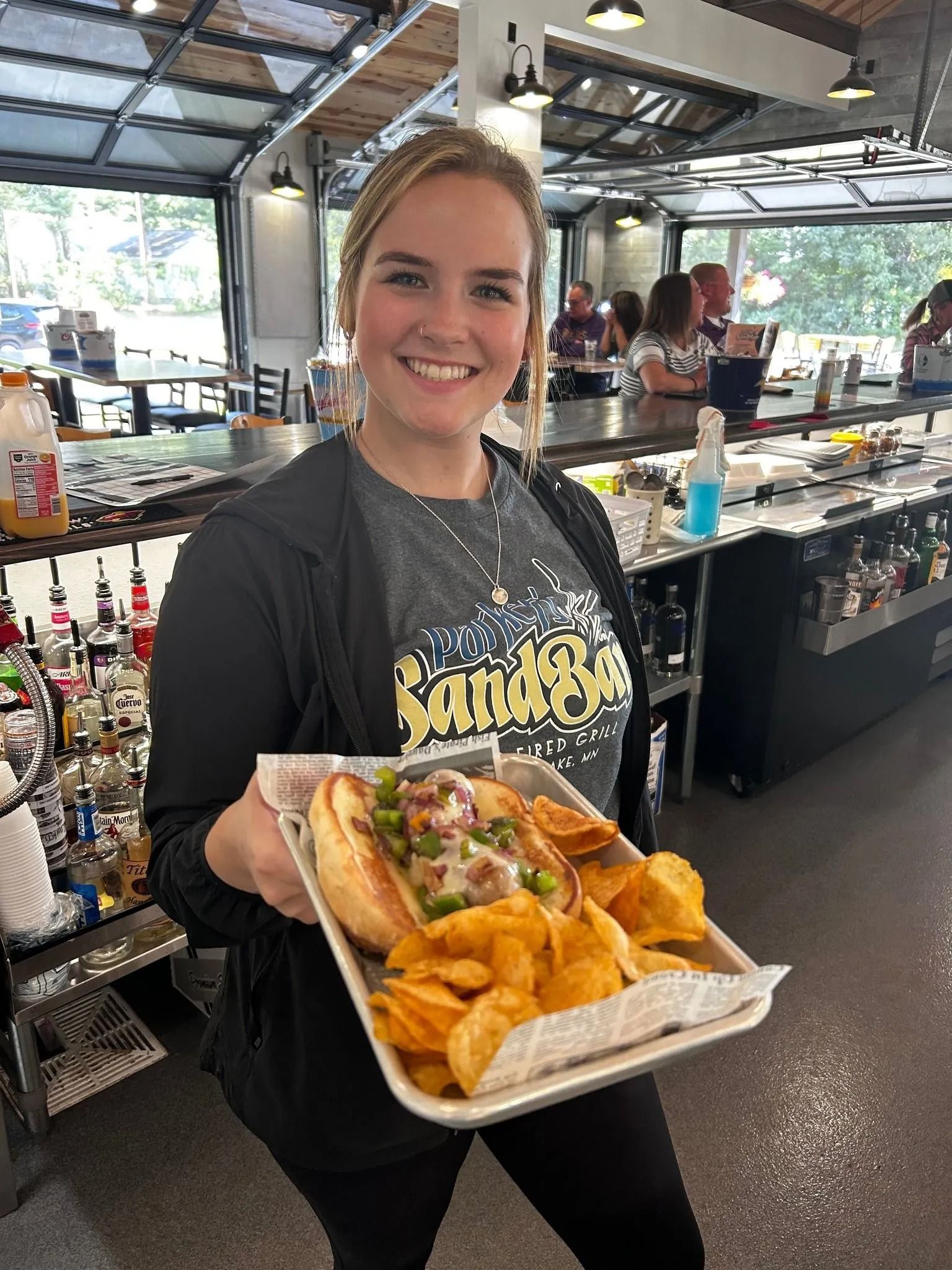 Woman in a bar area smiling and holding a tray with a sandwich and chips