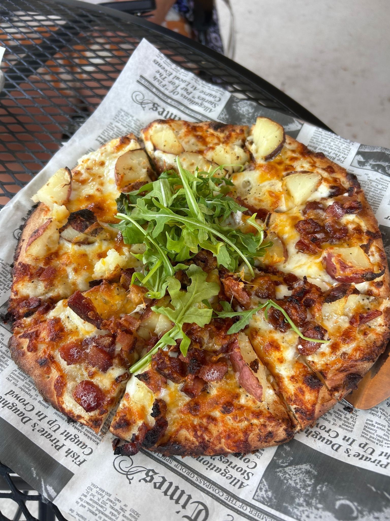Small pizza topped with arugula on a newspaper-lined tray, sliced into wedges.