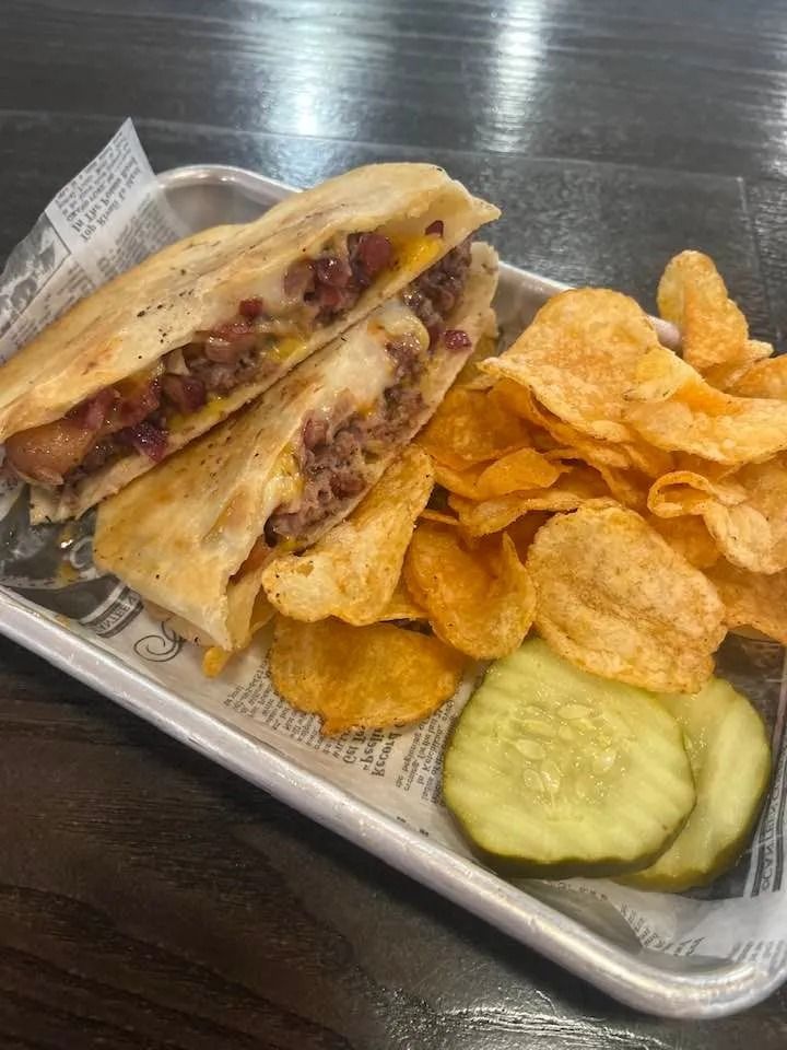 Grilled sandwich on a tray with potato chips and pickle slices