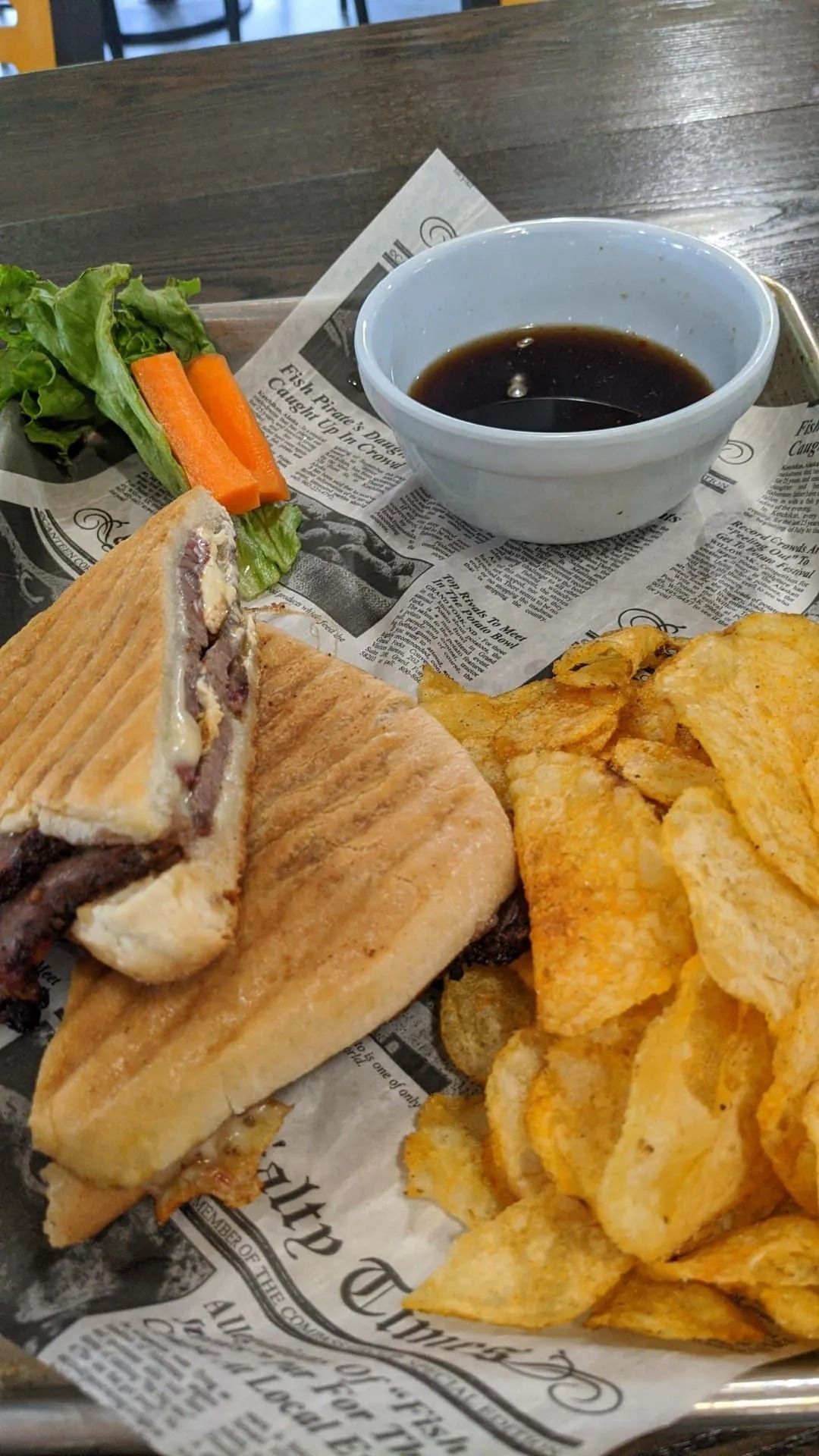 Sandwich and potato chips on newspaper-lined tray with dipping sauce and vegetables
