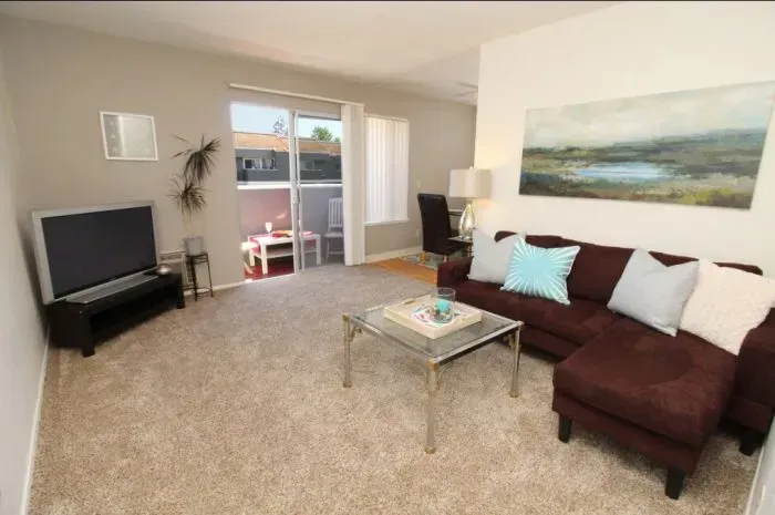 Living room with brown sectional sofa, TV, glass coffee table, and balcony.