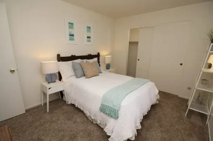 Bedroom with white walls, bed, nightstands, closet, and shelving unit.