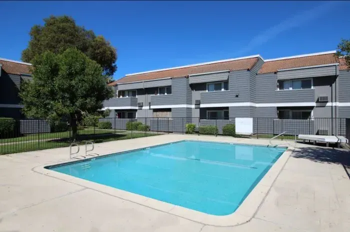 A swimming pool in front of a gray apartment building on a sunny day.