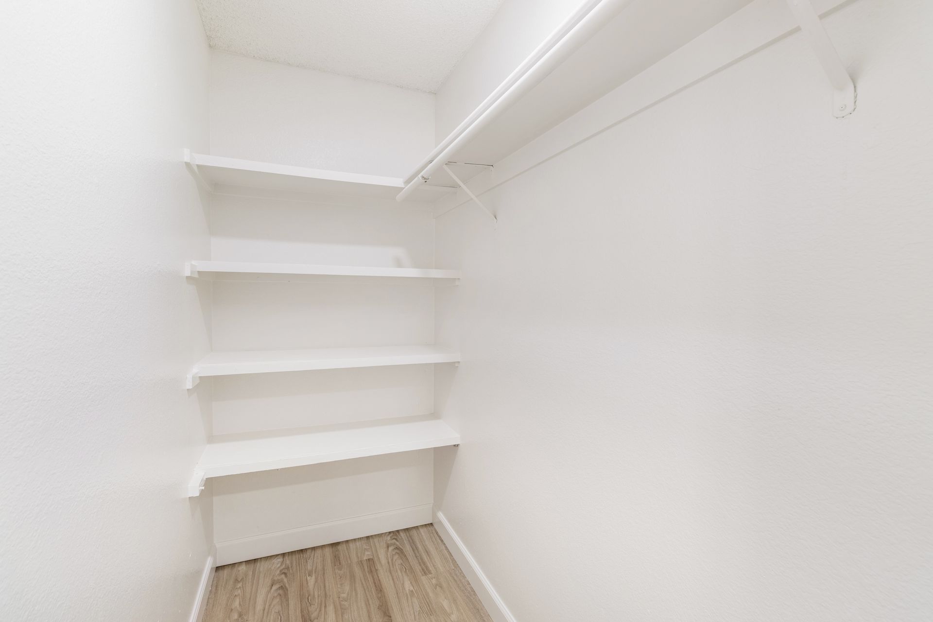 Empty white closet with shelves and a clothing rod.