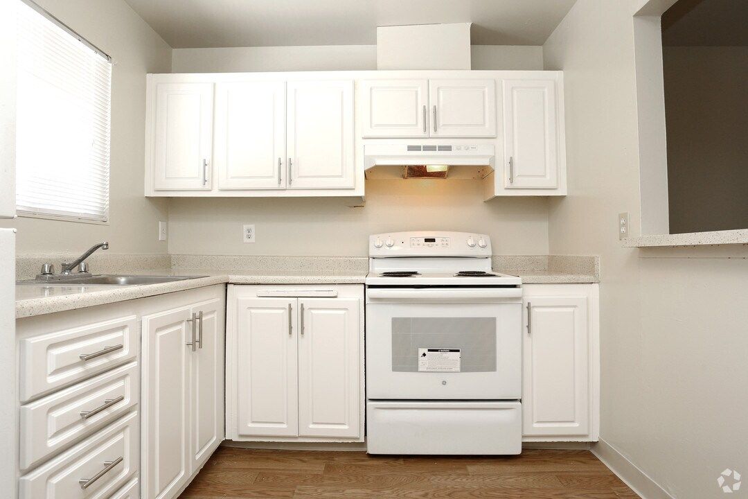 White kitchen with white cabinets, countertops, and appliances. A window is on the left, and a range hood above the stove.