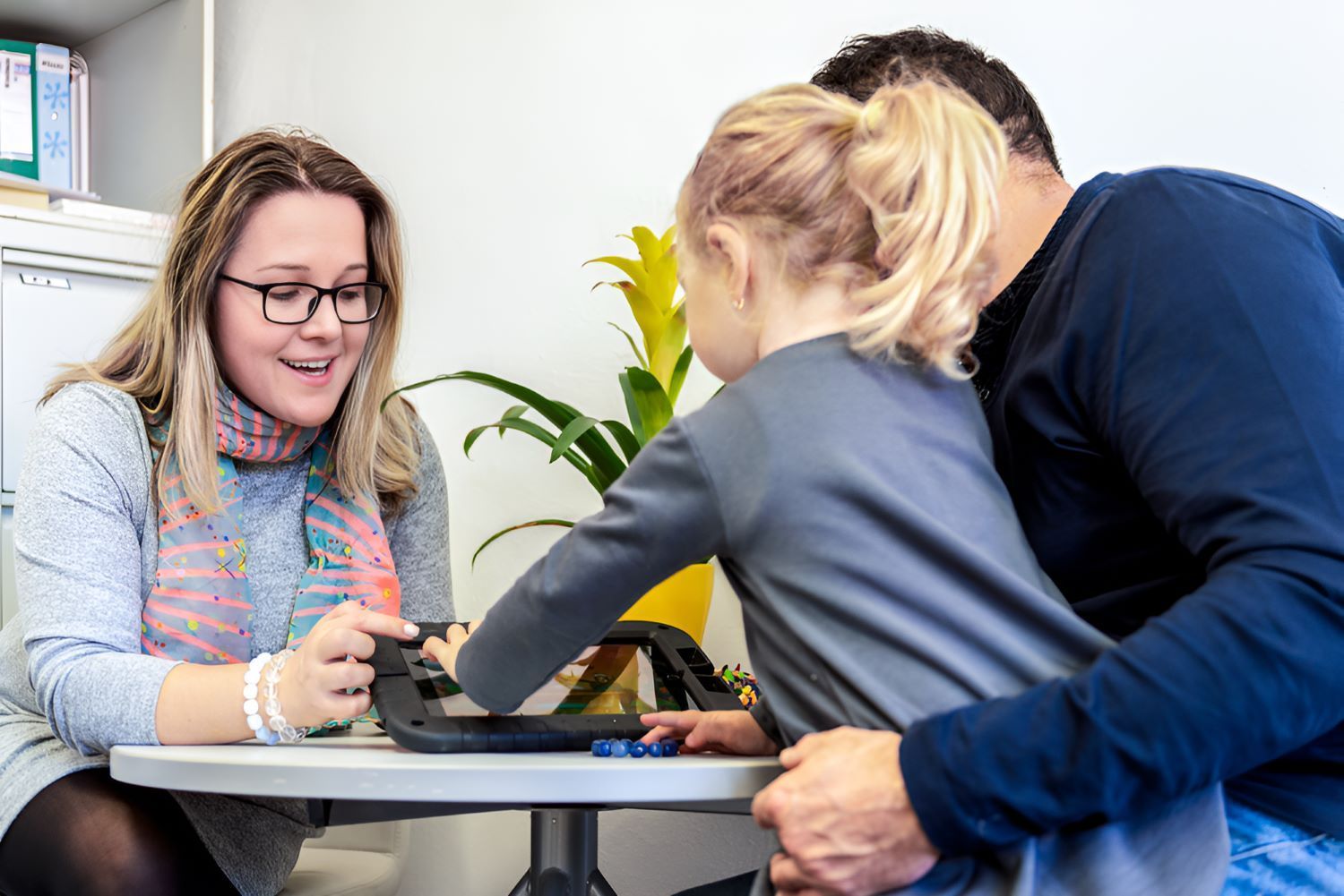 A Man and a Woman Are Sitting at a Table With a Little Girl — Newcastle Paediatric Occupational Therapy In Floraville, NSW