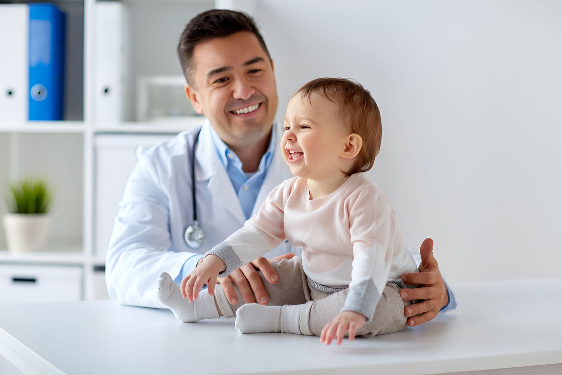 A Doctor is Holding a Baby Girl Who is Sitting on a Table — Newcastle Paediatric Occupational Therapy In Floraville, NSW