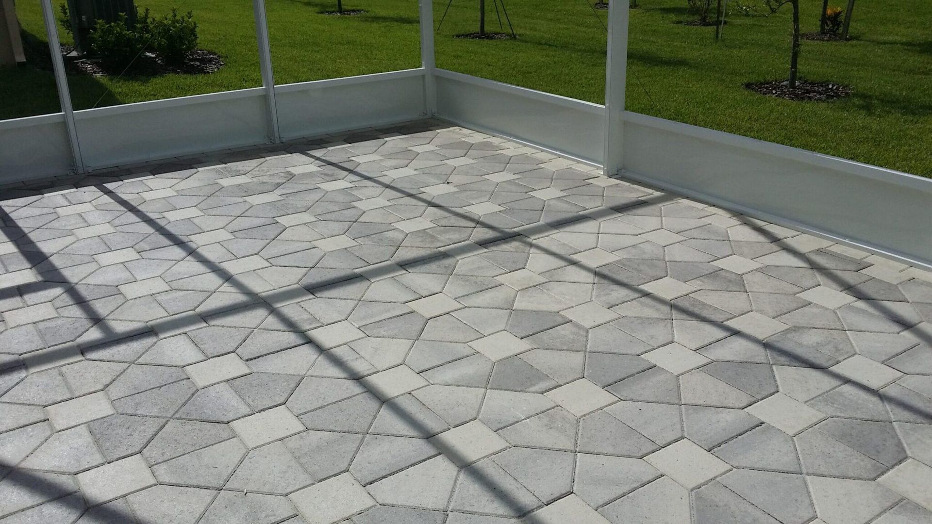 Gray stone patio with geometric pavers, bordered by low white fencing and green grass beyond.
