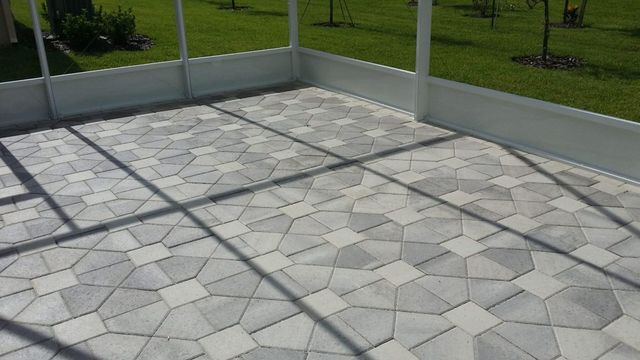 Gray stone patio with geometric pavers, bordered by low white fencing and green grass beyond.