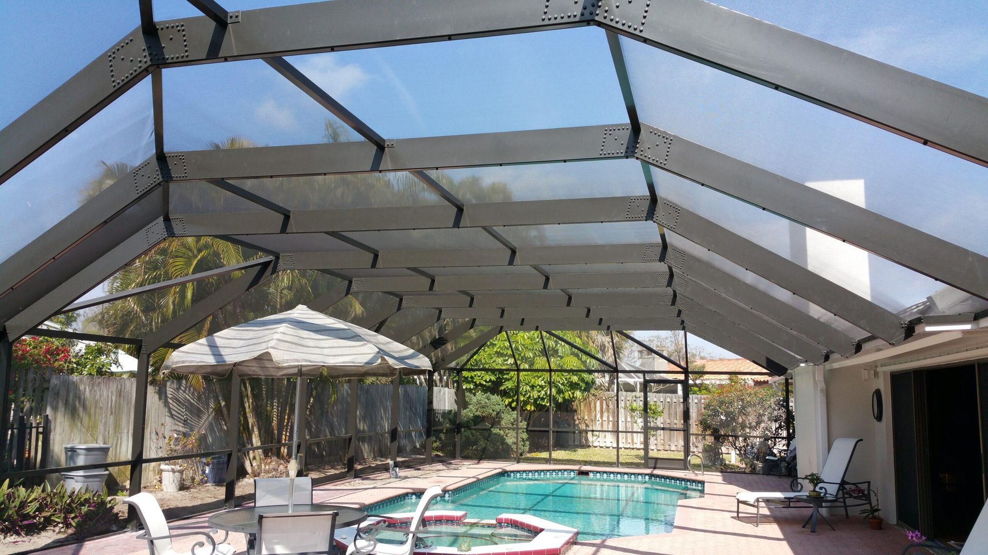 Covered backyard pool with white screen enclosure, patio furniture, and trees in the background