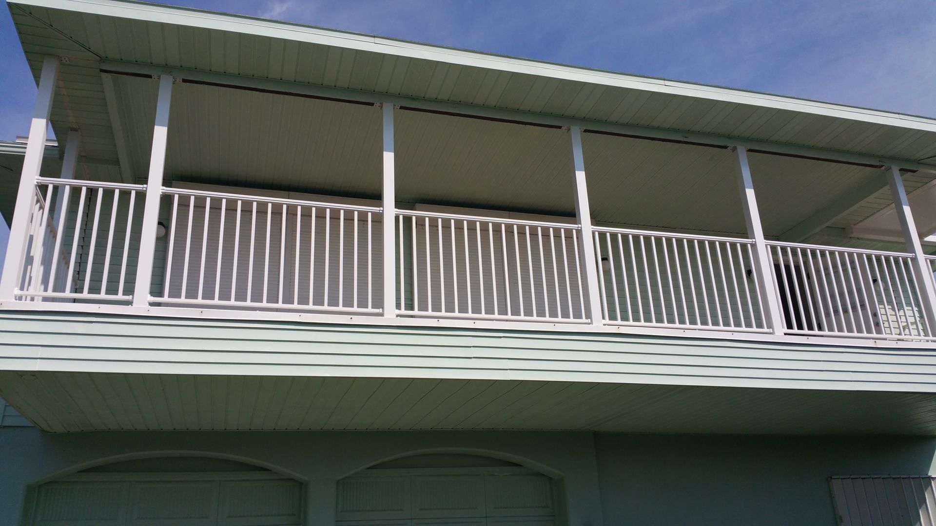White balcony with railings and green siding on a house.