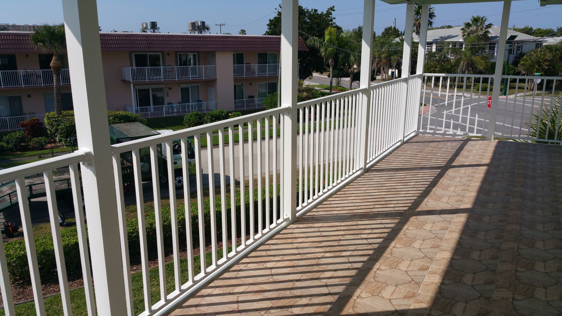 White-railed walkway overlooking a courtyard and pink apartment buildings, with striped sunlight on the floor