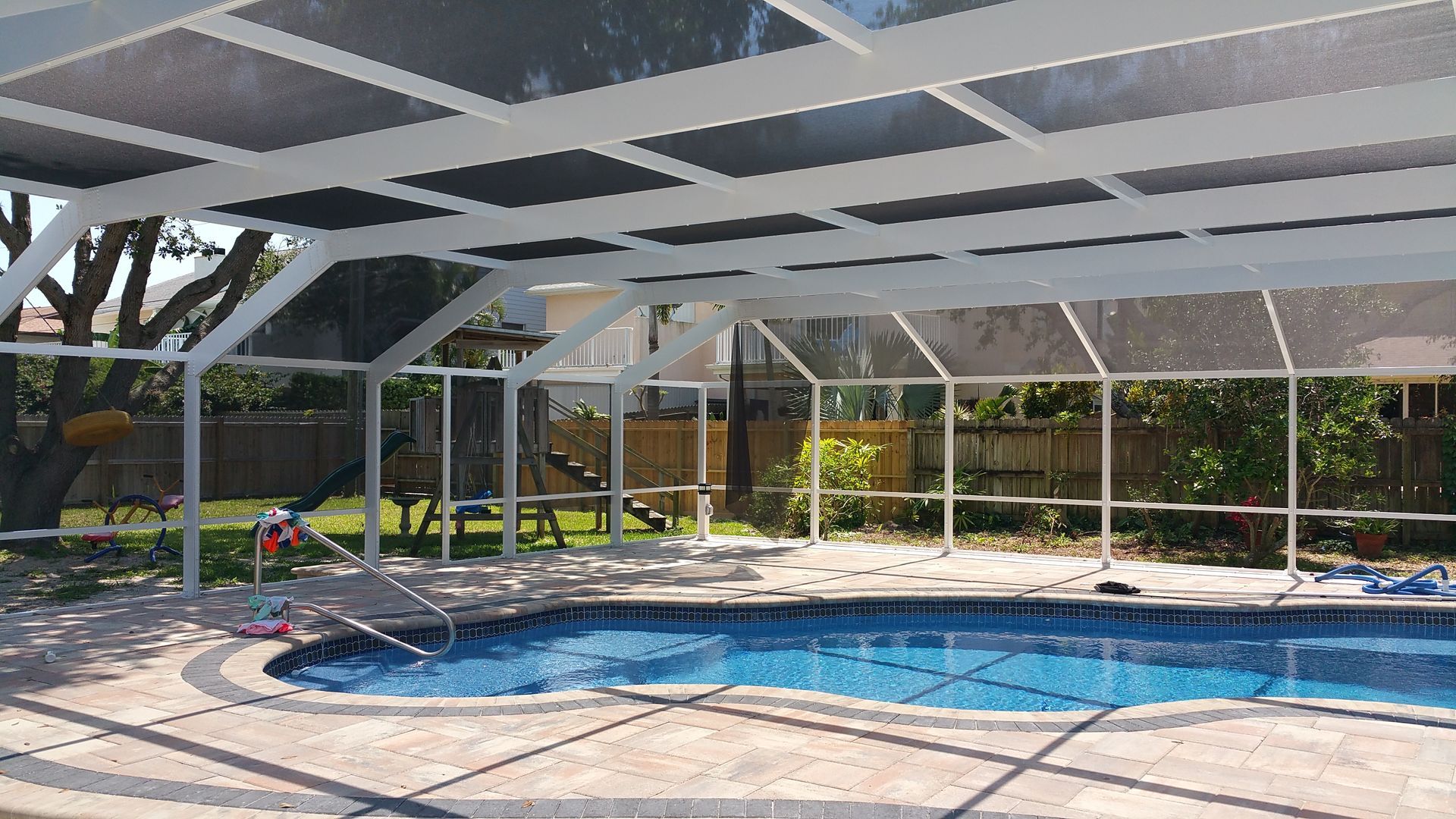 Covered backyard patio with a screened-in pool and white beams in bright sunlight