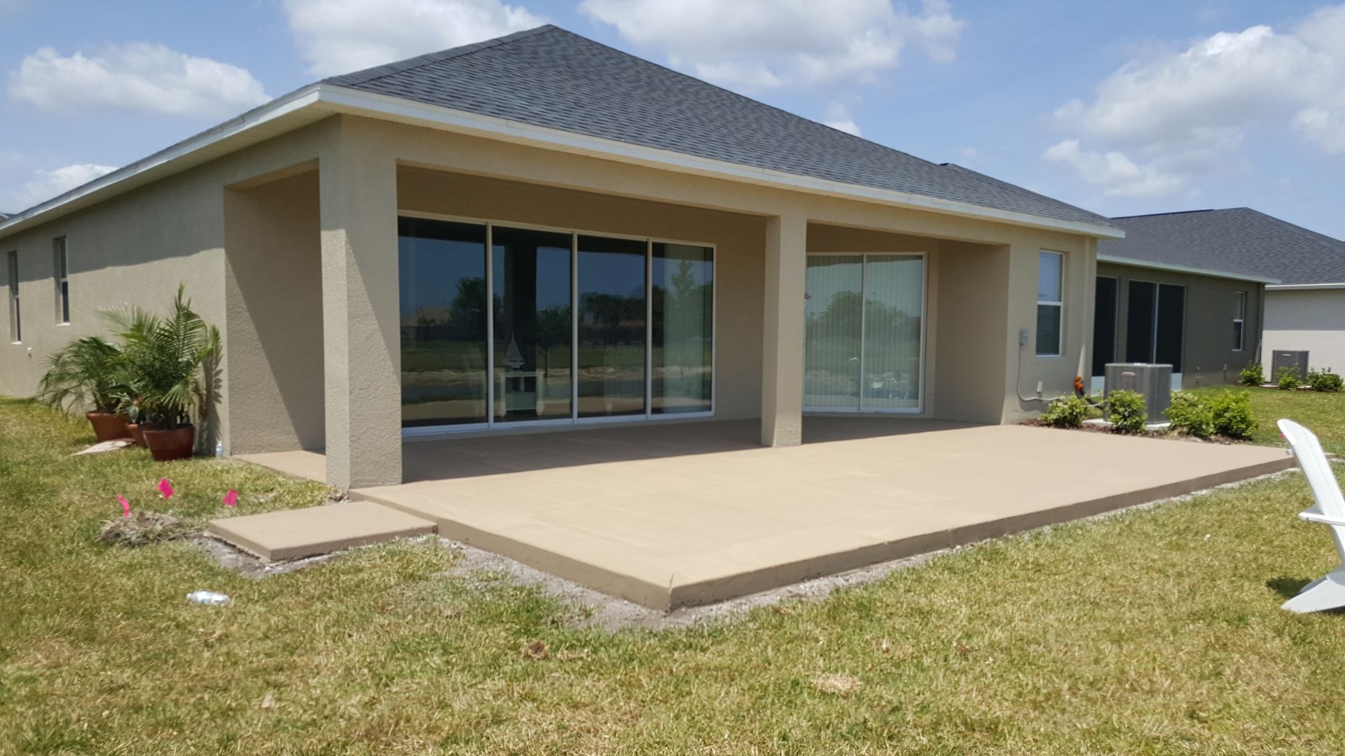 Modern beige house with a covered patio, large sliding glass doors, and a grassy yard