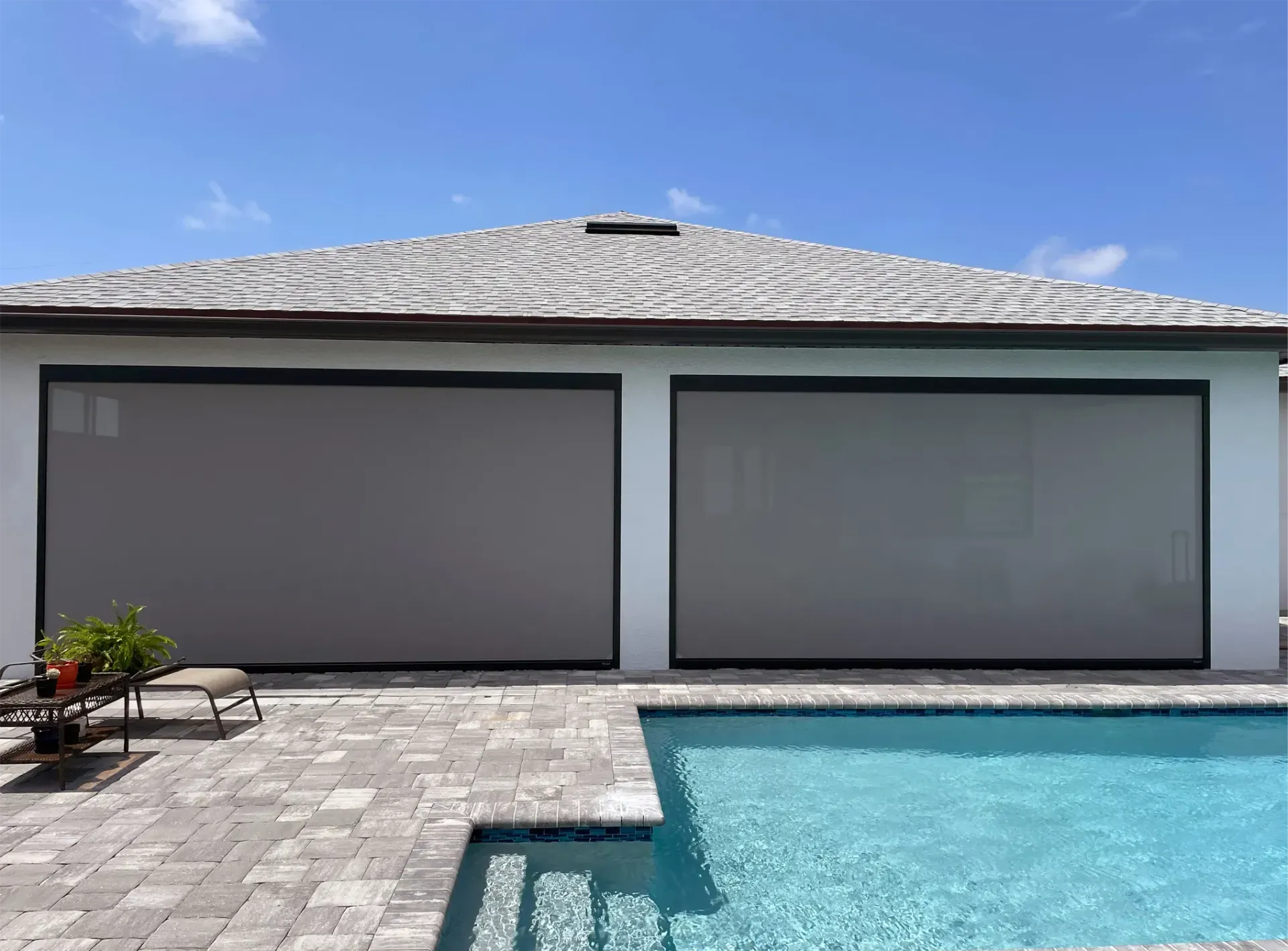 Modern house patio with closed gray roller shades and a blue swimming pool under a clear sky