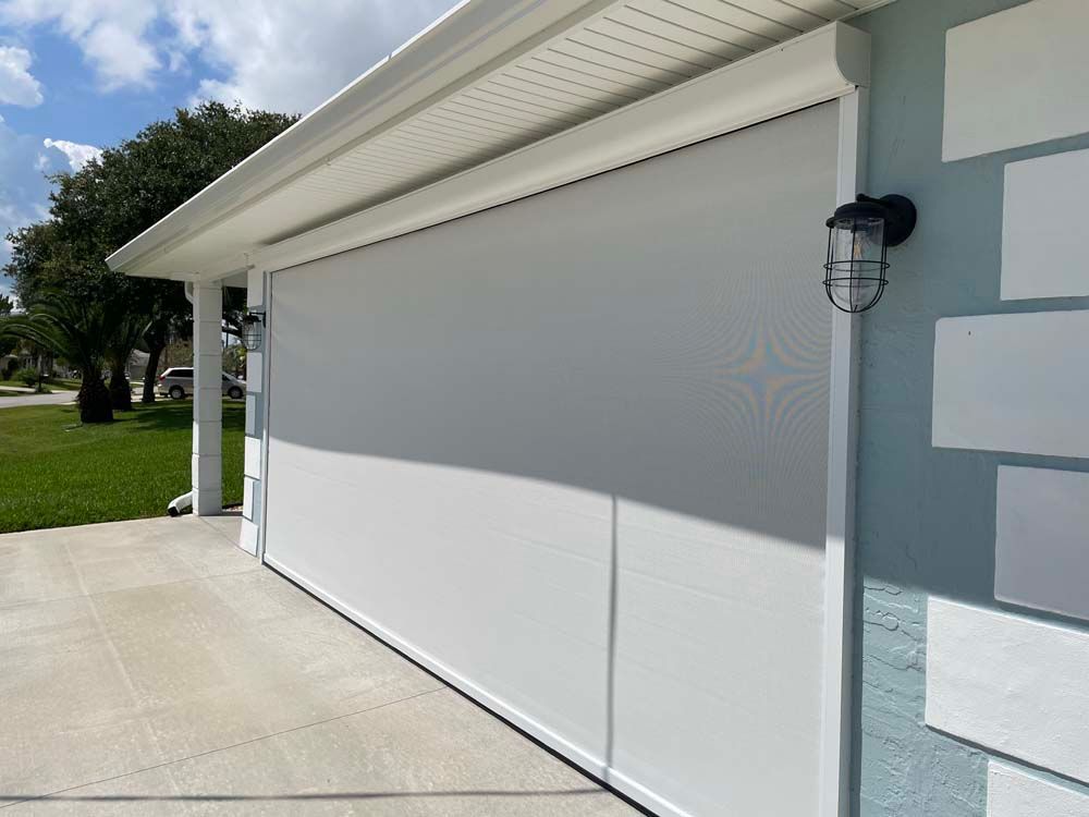 Closed white garage door on a light gray house with a wall light and driveway in front.
