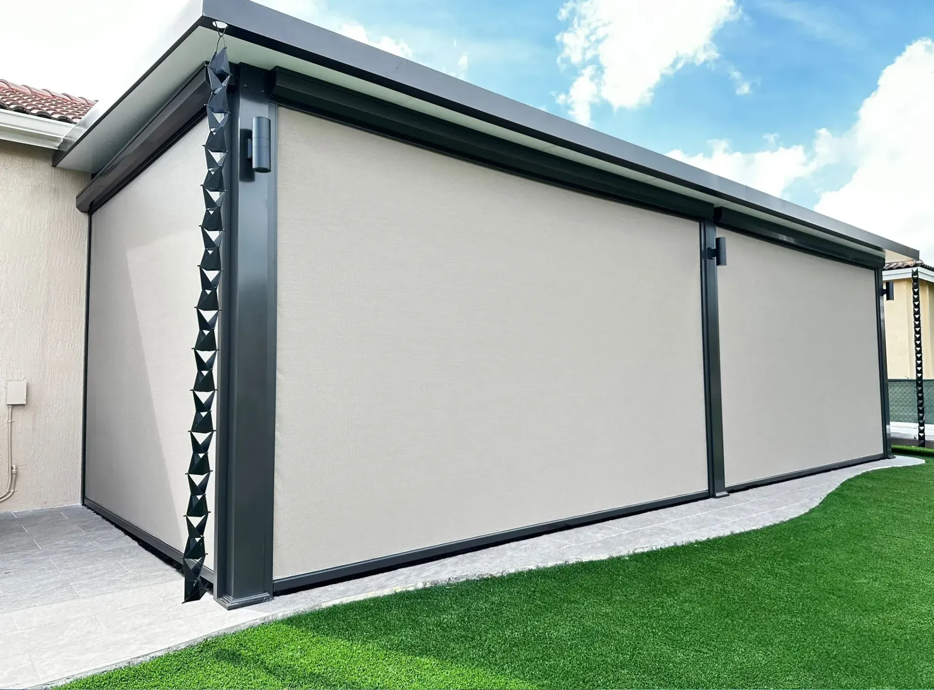 Side view of a beige exterior wall with black trim and a green lawn beneath a partly cloudy sky
