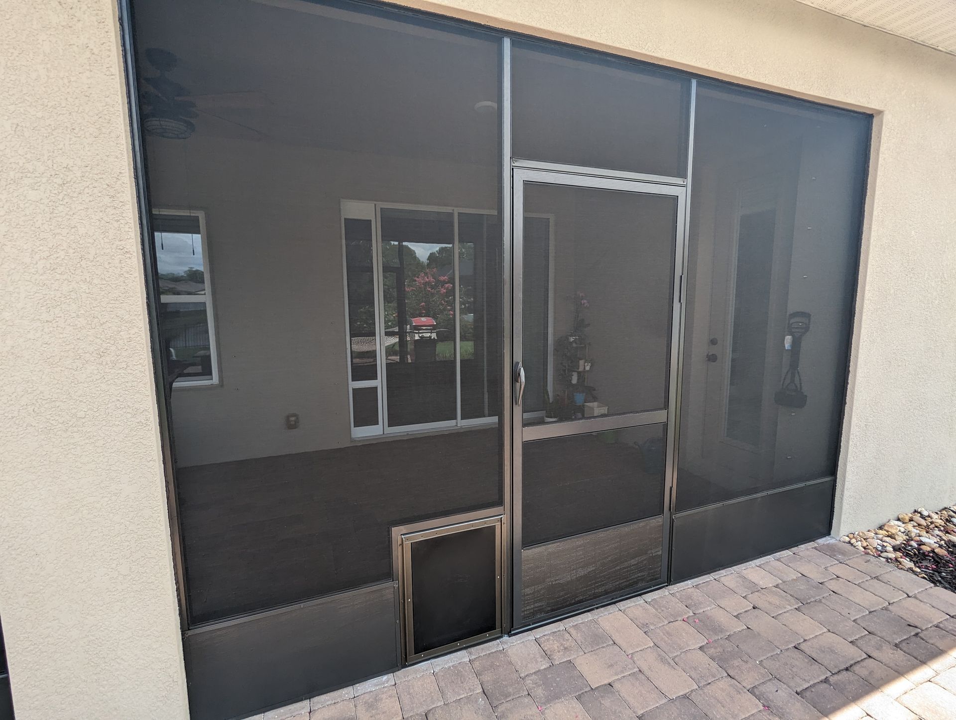 Dark-tinted glass storefront or patio enclosure with a screened door and stone paver walkway.