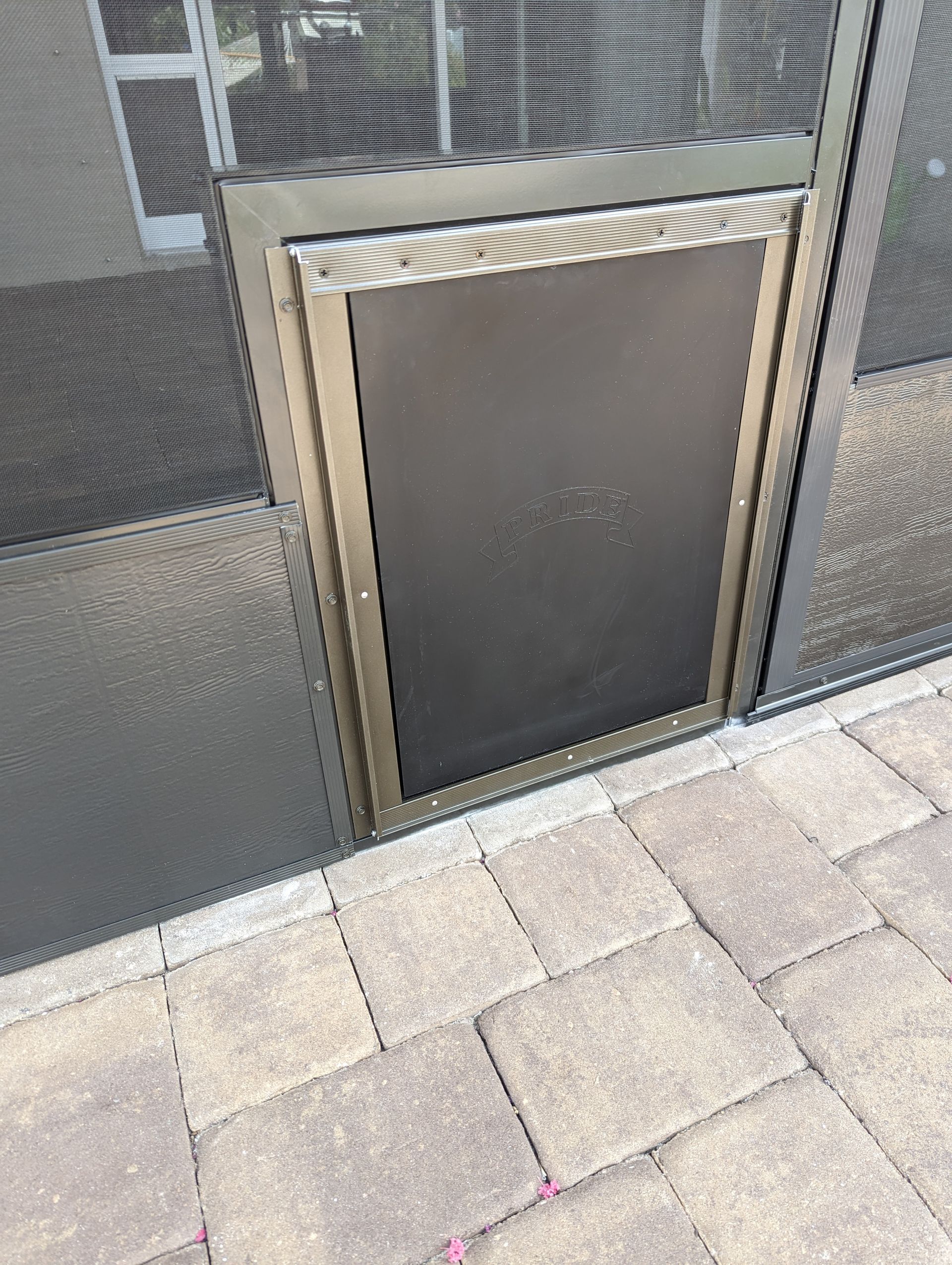 Small black access door set in a metal wall above stone pavement.
