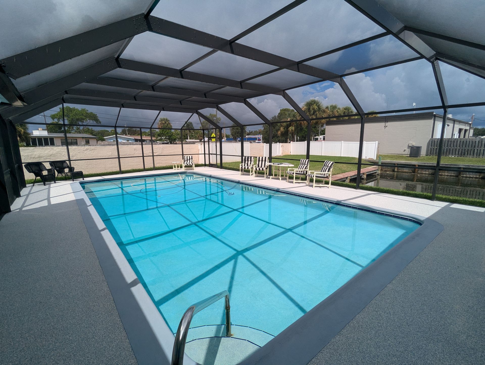 Screened patio with pool, palm trees, and a cloudy ocean view beyond