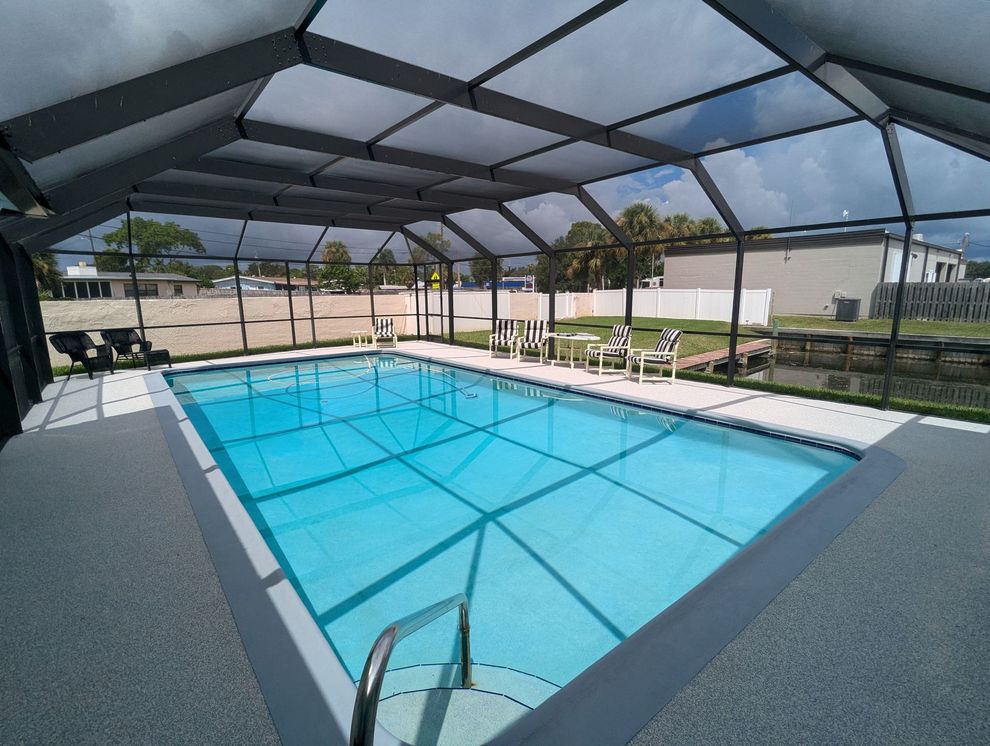 Screened-in outdoor pool with blue water and white lounge chairs under a mesh enclosure.