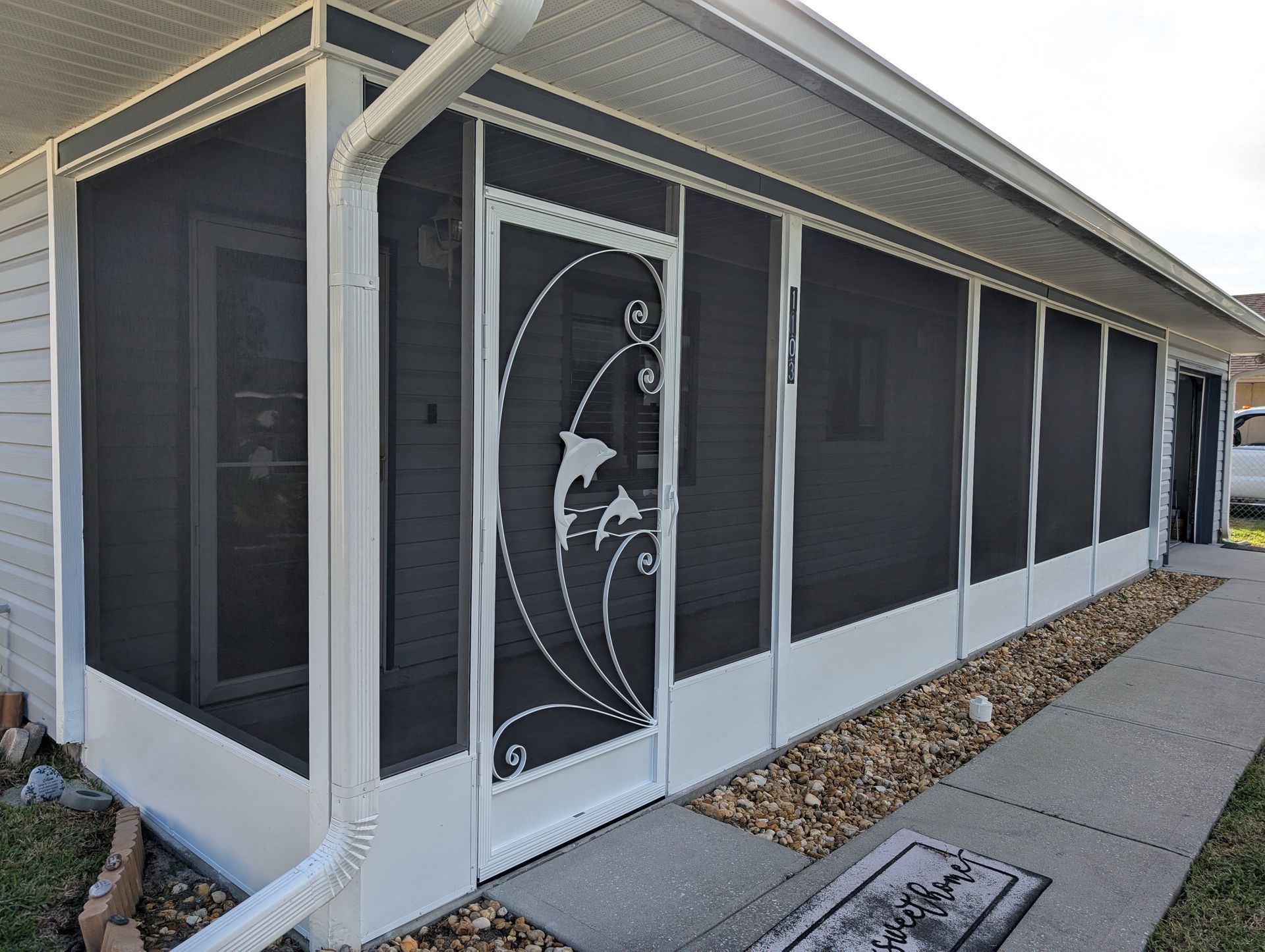 White screened porch with decorative glass storm door beside a concrete walkway and gravel border