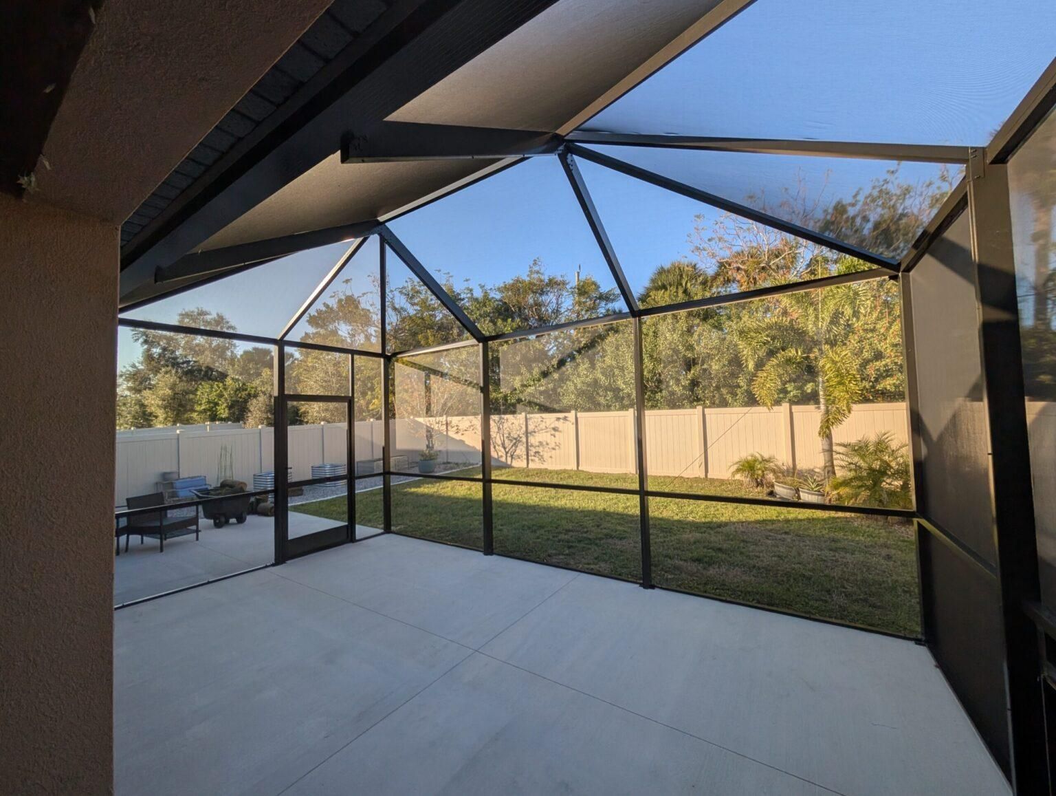 Covered patio with screened enclosure, concrete floor, and grassy backyard with trees and privacy fence