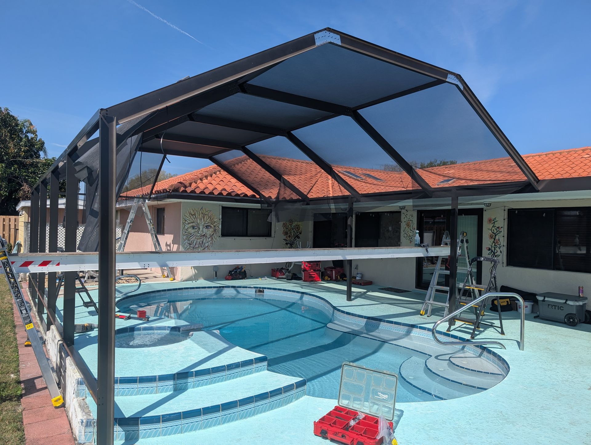 Outdoor swimming pool with a black shade canopy and lounge chairs beside a house with a red-tiled roof