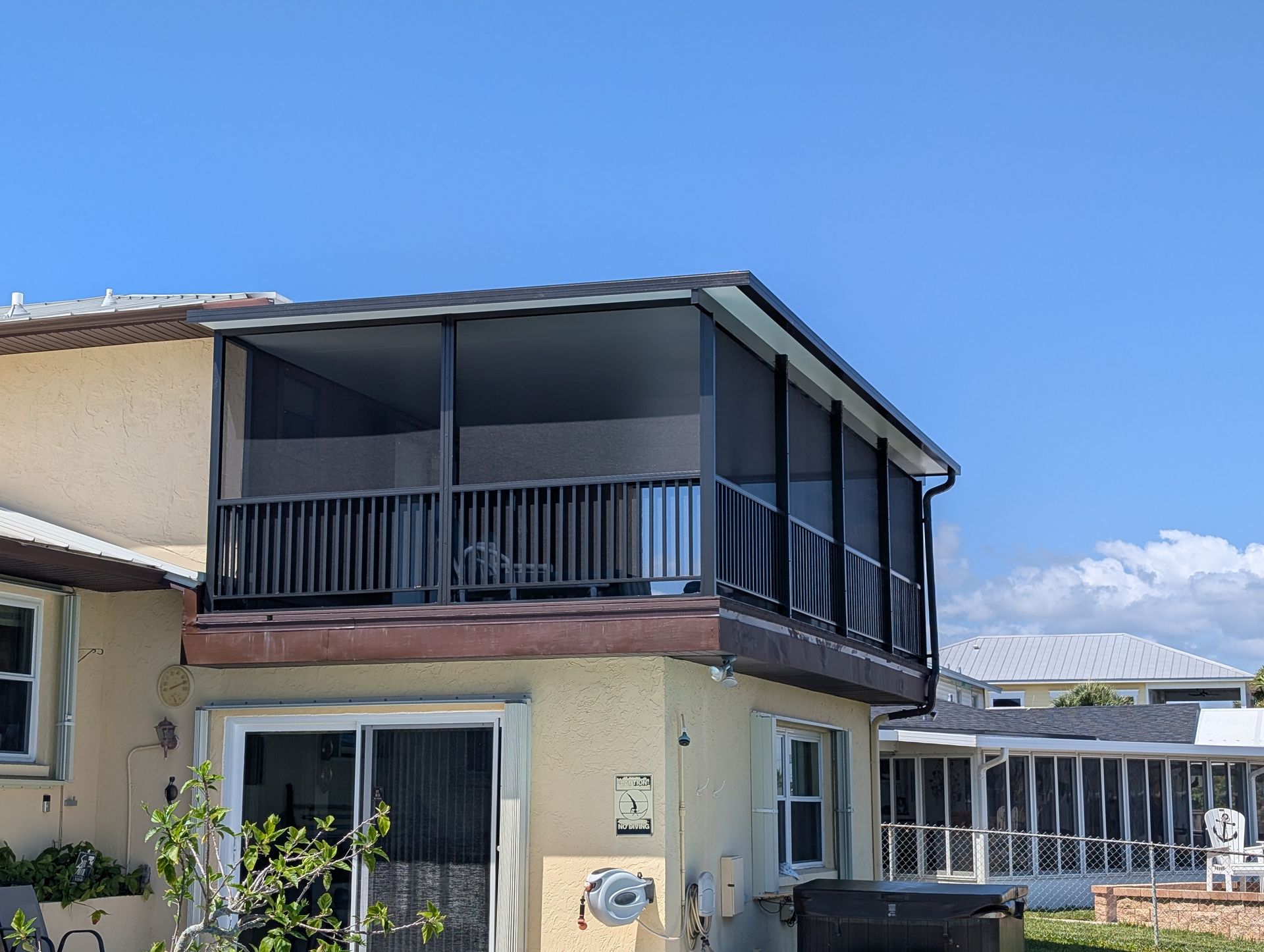 Two-story beige house with a dark screened balcony and patio under a clear blue sky